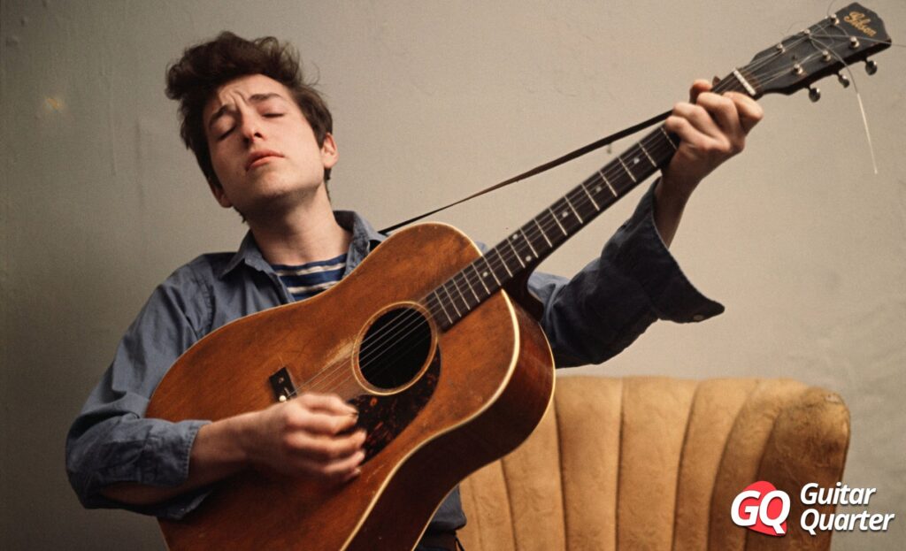 Un joven Bob Dylan con una guitarra acústica Gibson muy desgastada.
